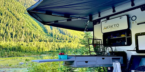 Arkto Campers outdoor kitchen setup under awning beside mountain lake